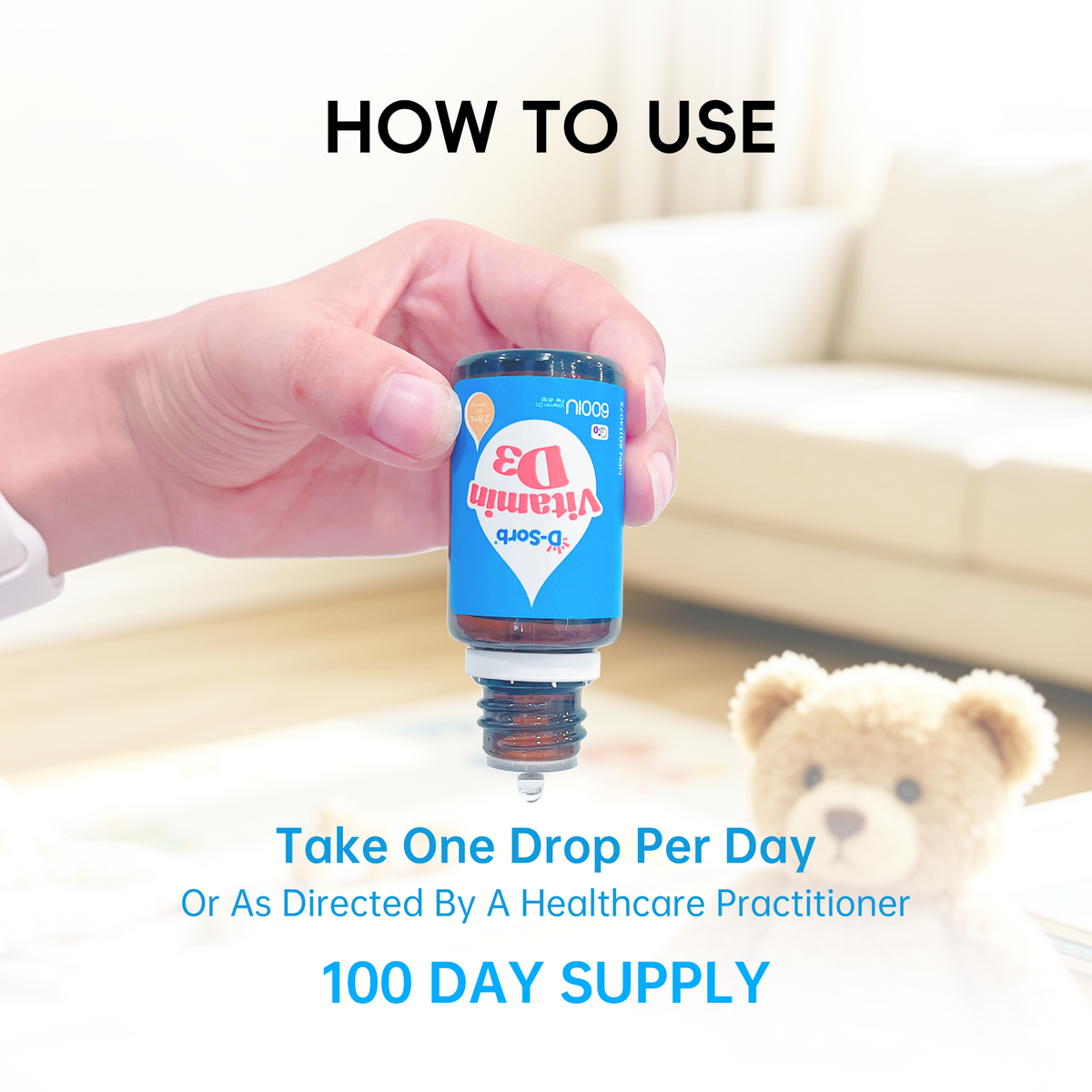 A hand holds a small amber bottle labeled Vitamin D3 Soft in front of a blurred living room background with a teddy bear. Text reads 'HOW TO USE' and 'Take One Drop Per Day Or As Directed By A Healthcare Practitioner 100 DAY SUPPLY'.
